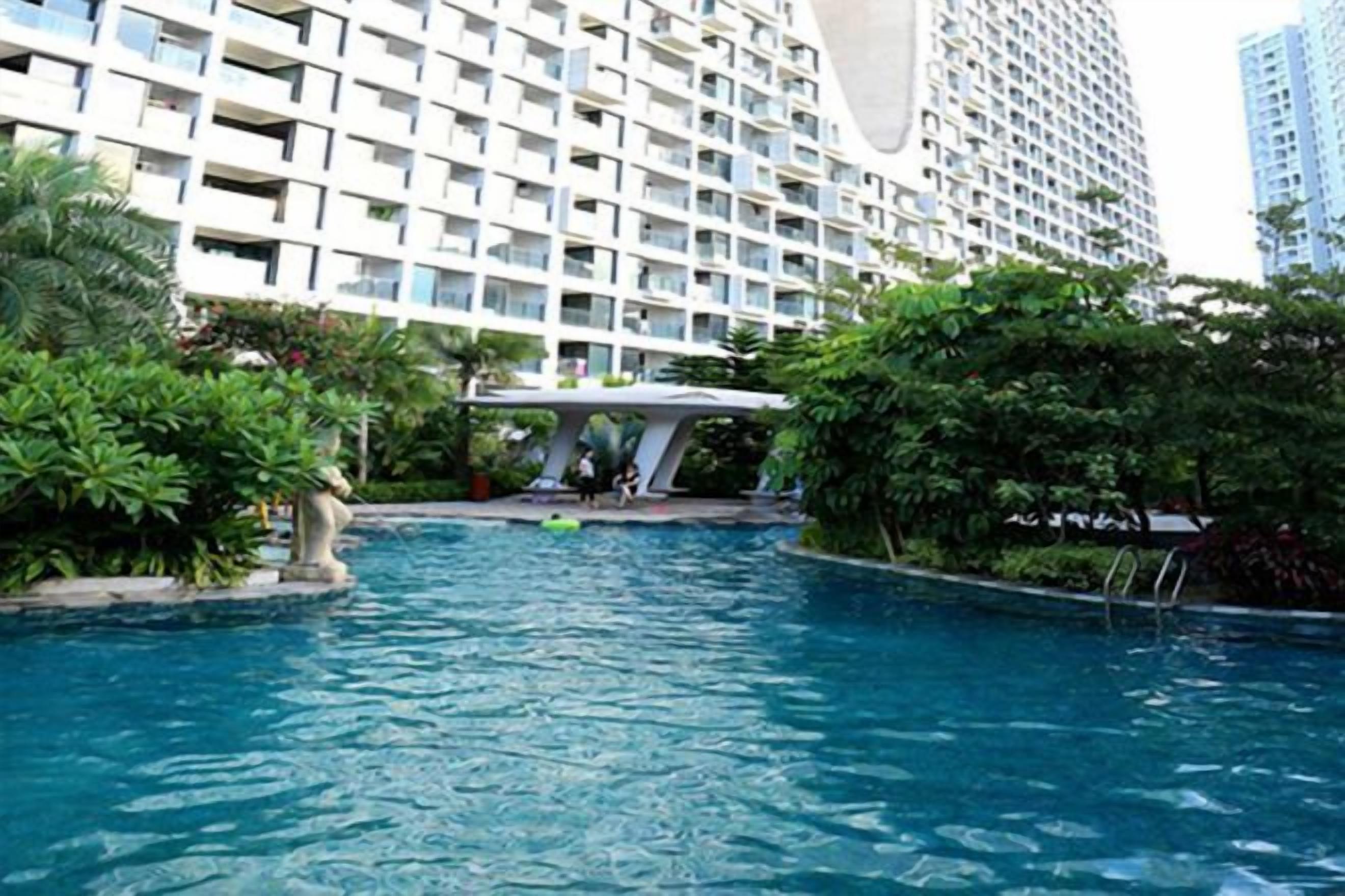 A swimming pool surrounded by greenery and a modern building with balconies.