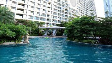 A swimming pool surrounded by greenery and a modern building with balconies.