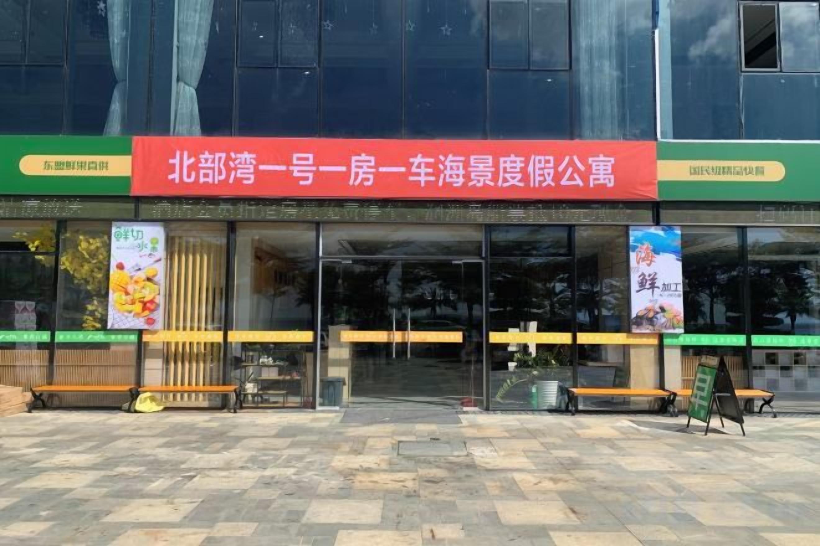 A building with a red sign, glass doors, and a bench outside.