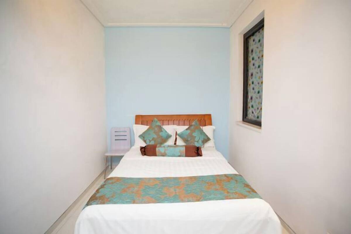 Une chambre d’hôtel étroite, avec un lit, une table de chevet et une fenêtre donnant sur un paysage agréable.