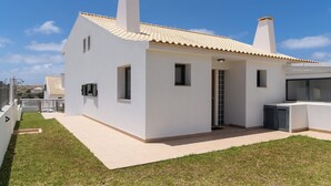 Une maison moderne, blanche, avec un toit en tuiles, un petit porche à l’avant et une cheminée bien visible.