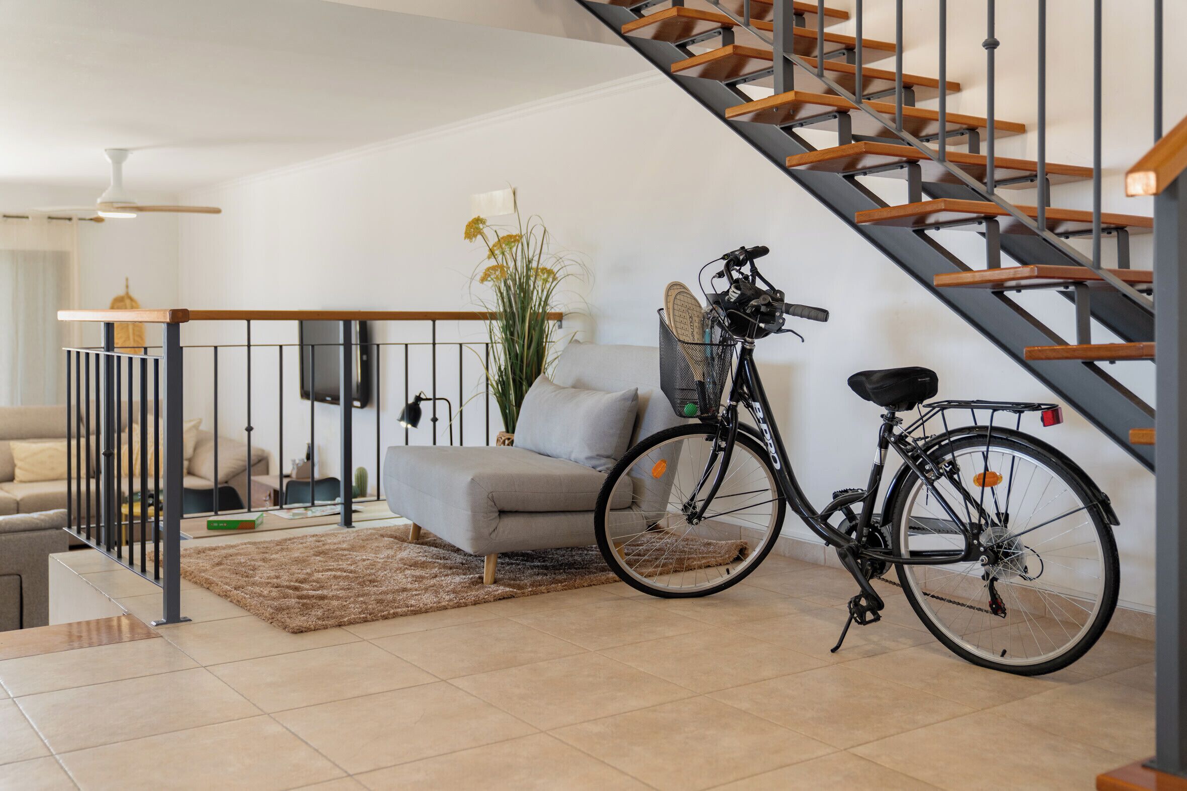 Ein modernes Wohnzimmer mit Treppe, einem grauen Sofa, einem Couchtisch und einem Fahrrad.