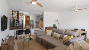 Un salon moderne doté d’un grand canapé d’angle, d’un coin repas avec une table et des chaises en bois, et d’un escalier menant à un niveau supérieur.