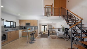 Une cuisine moderne avec un îlot central, un coin repas doté d’un canapé et un escalier menant à un niveau supérieur.