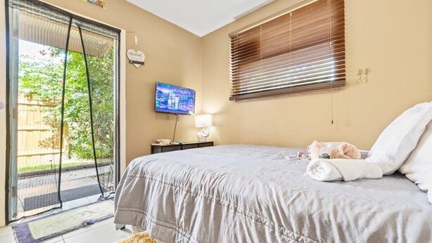 A bedroom with a bed, a TV, a window with blinds, and a door leading to a balcony. - Modern comfortable close to the beach/airport (Fort Lauderdale)