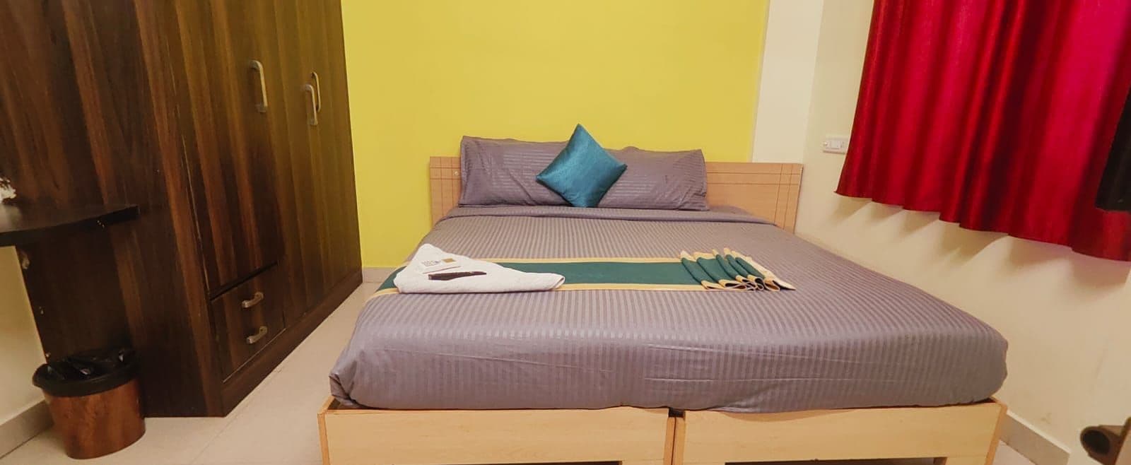 A room with a bed, wooden wardrobe, and a red curtain.