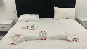 Une chambre d’hôtel avec un grand lit, du linge de lit blanc et une tête de lit noire. Il y a deux tables de chevet avec des lampes.