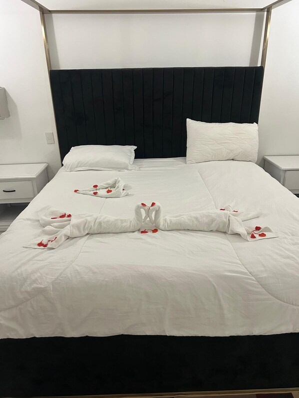 Habitación de hotel con una cama grande, ropa de cama blanca y cabecera negra. Hay dos mesitas de noche con lámparas.