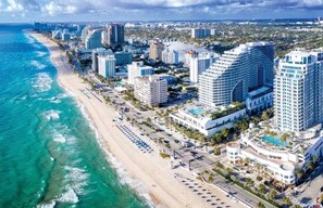 A coastal cityscape with a beachfront hotel featuring a pool, multiple buildings, and a clear view of the ocean.