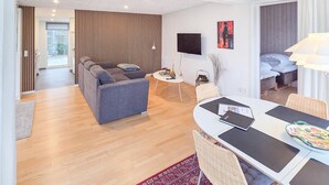 A modern living room with a grey sofa, a dining table with chairs, a TV mounted on the wall, and a bed in the adjacent room. - Gorgeous home in Broager with WiFi (Broager)
