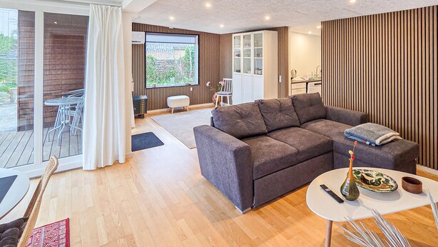 A modern living room with a grey sofa, a dining table with a vase and remote control, and a view of the outdoors through large windows. - Gorgeous home in Broager with WiFi (Broager)