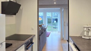 A modern kitchen with a built-in stove, a dining area with a sofa and table, and a view of the backyard through large sliding doors. - Gorgeous home in Broager with WiFi (Broager)