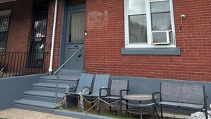 A two-story brick house with a front porch, a covered entryway, and a small outdoor seating area with a table and chairs.