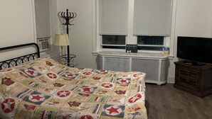 A bedroom with a bed, a lamp, a TV, and a window with blinds.