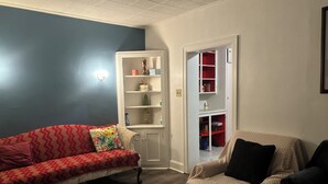 A living room with a red sofa, a beige armchair, and a white shelving unit against a blue wall.