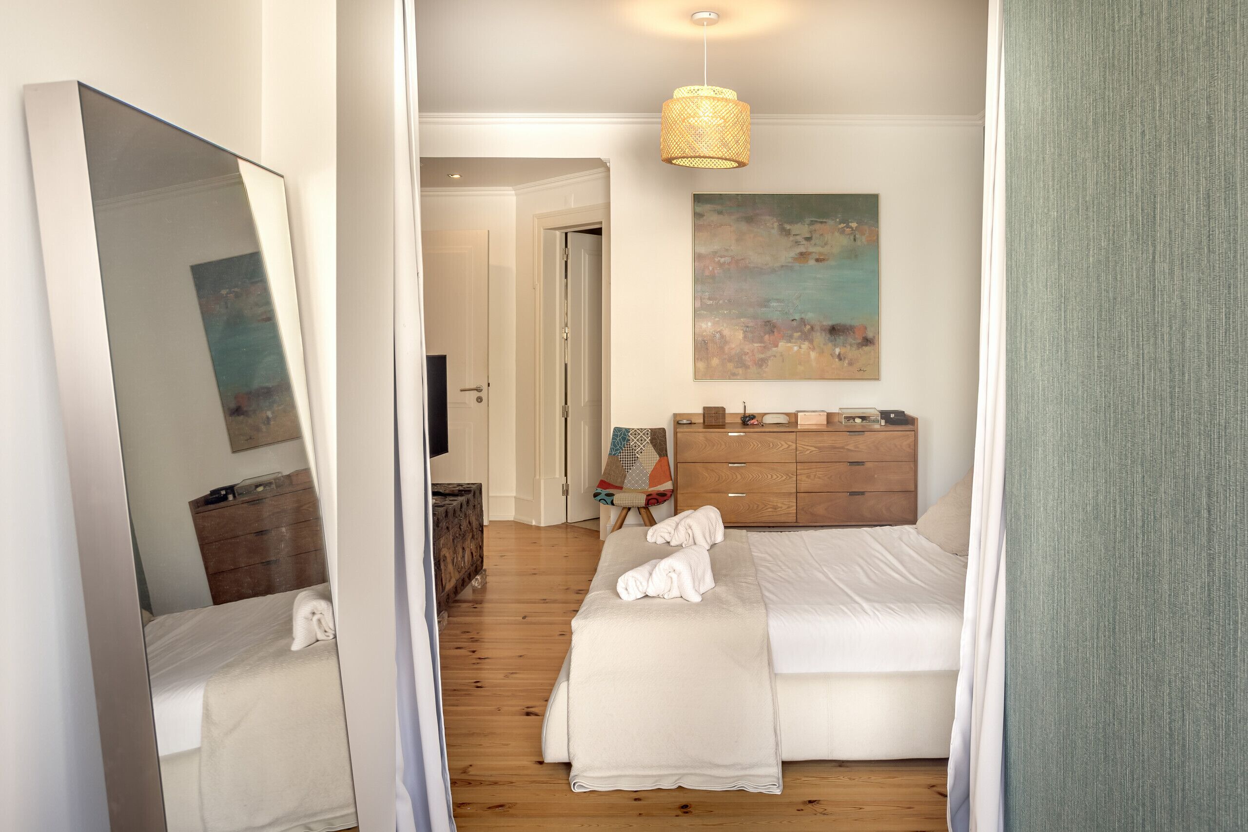 Ett hotellrum med en säng, en byrå i trä, en tavla på väggen och en spegel.