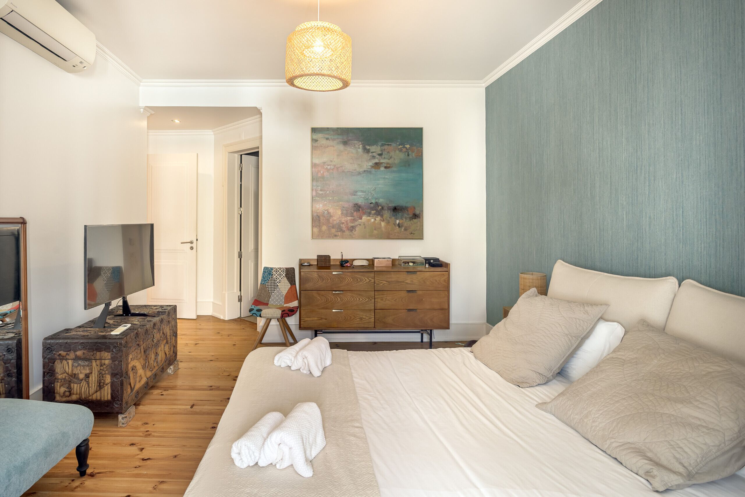 Ein Schlafzimmer mit einem großen Bett, einem Schminktisch, einem Fernseher und einem Gemälde an der Wand.