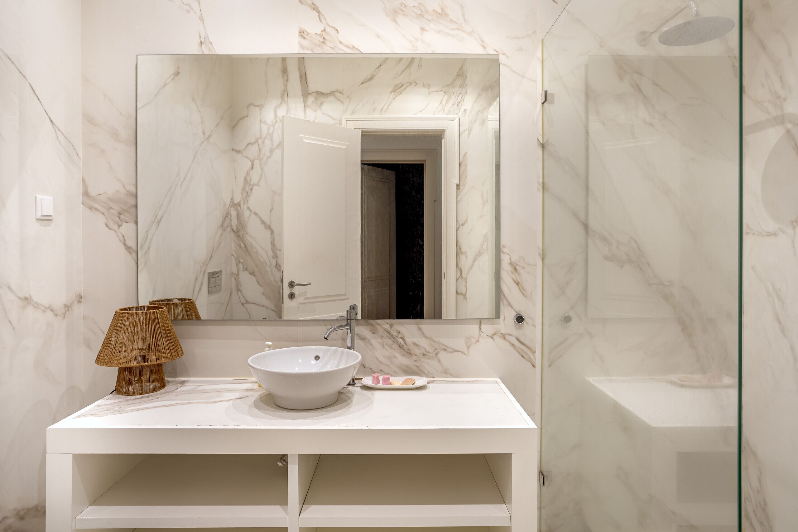 Un bagno moderno con un lavabo in marmo bianco, uno specchio grande e un box doccia in vetro.