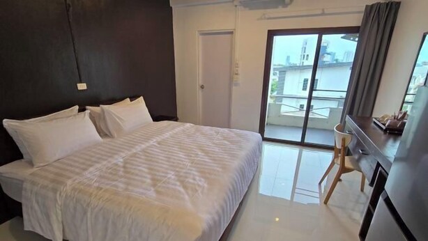 A bedroom with a bed, a desk, a chair, and a sliding glass door to a balcony. - J.K. Mansion (Bangkok)