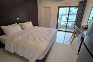 A bedroom with a bed, a desk, a chair, and a sliding glass door to a balcony. - J.K. Mansion (Bangkok)