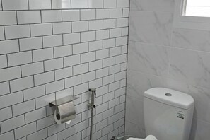 A bathroom with white tiled walls, a toilet, and a paper towel dispenser. - J.K. Mansion (Bangkok)