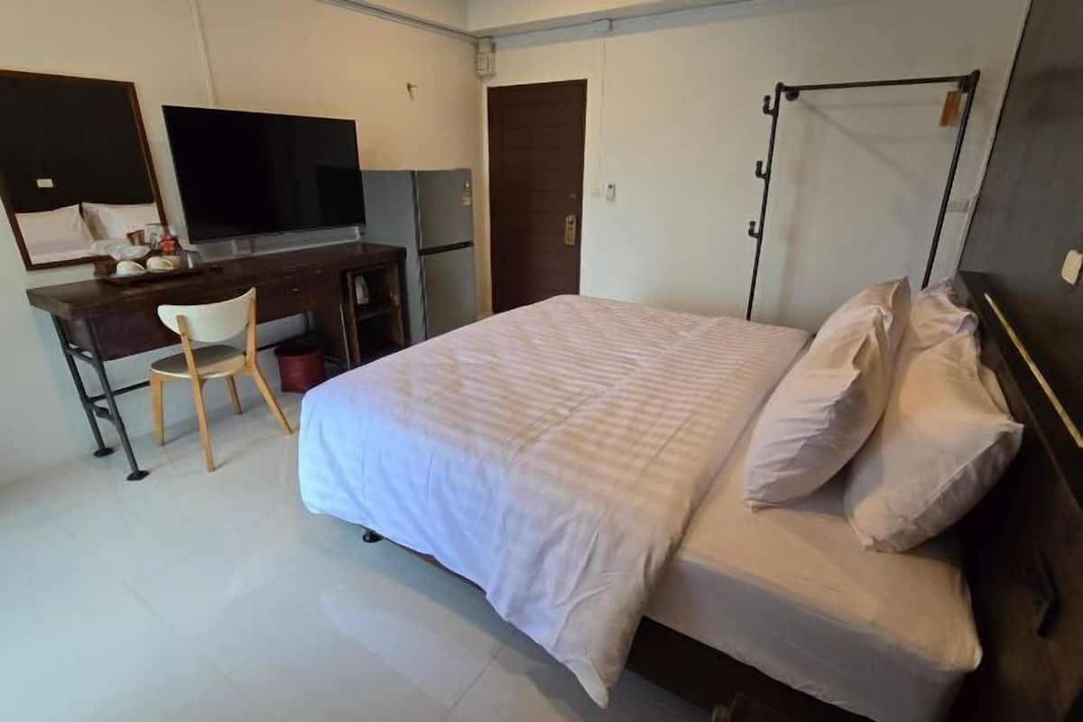 A hotel room with a bed, a desk with a chair, a television, and a wardrobe.