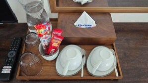 A tray with a remote control, two glasses, a water bottle, a bowl of coffee creamer, two packets of Nescafe coffee, and two white plates with spoons. - J.K. Mansion (Bangkok)