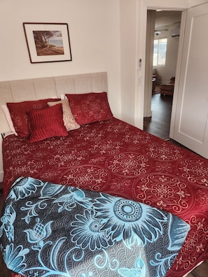 Een bed met een rood gebedruid sprei, een hoofdbord en een ingelijst schilderij aan de muur.
