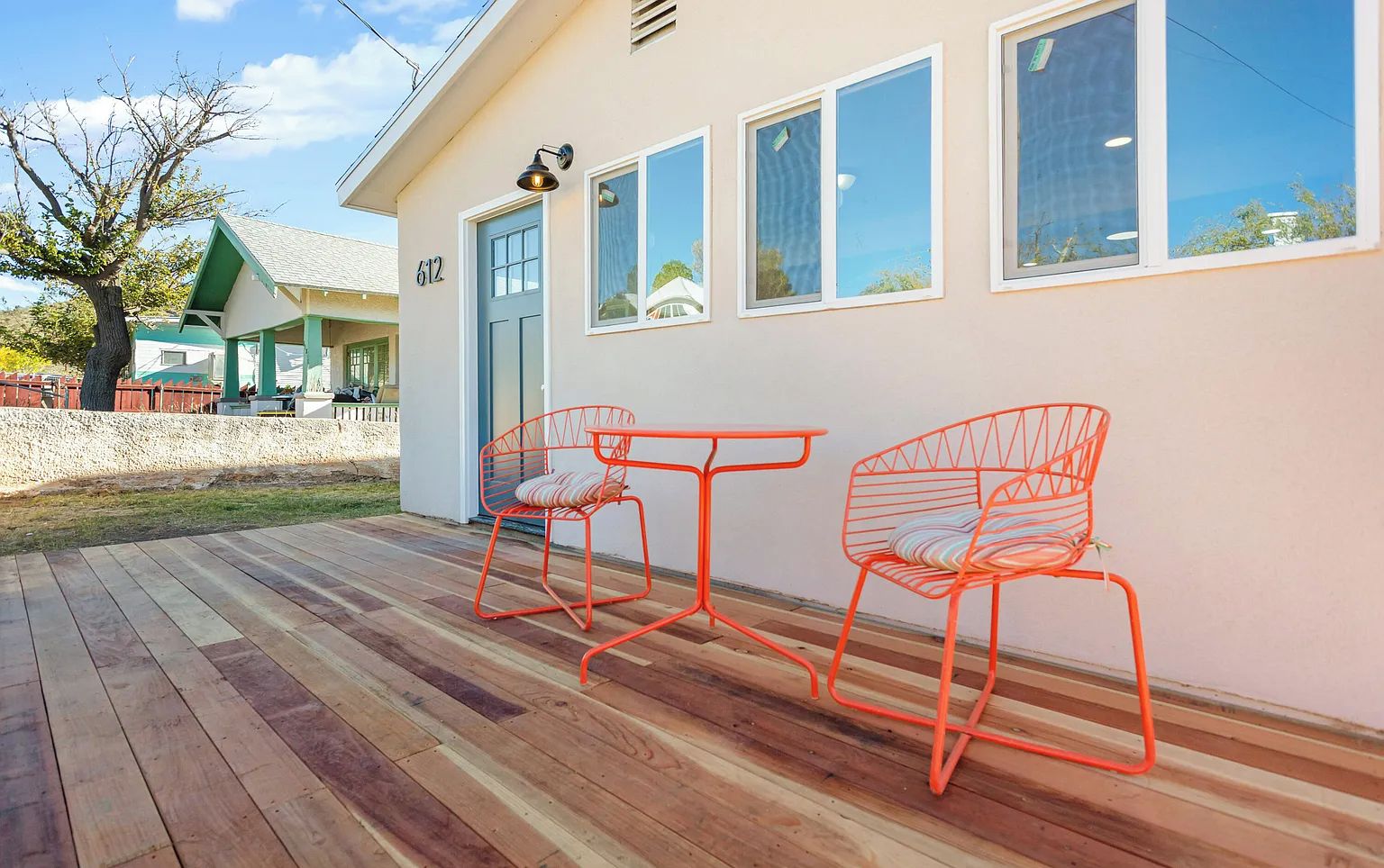 A house with a wooden deck, two orange wire chairs, and a small table.