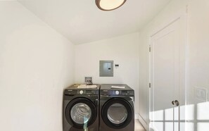 A laundry room with two Samsung washing machines, a light switch, and a door.