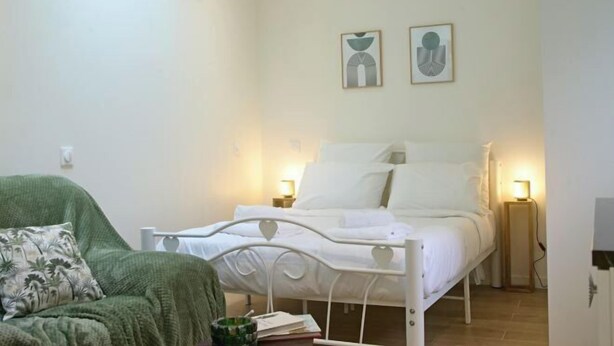 A bedroom with a white metal bed frame, a green armchair, and two bedside lamps. - Montparnasse 2 - Studio (Paris)