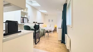 Eine moderne Küche mit Kaffeemaschine, ein Essbereich mit Tisch und Stühlen sowie ein Schlafzimmer mit Bett und Fenster.