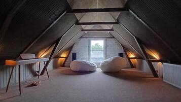 An attic bedroom with a sloped ceiling, a small table, two bean bags, and a window providing natural light.