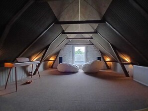 An attic bedroom with a sloped ceiling, a small table, two bean bags, and a window providing natural light. - Cosy and modern house in peaceful setting (Otterup)