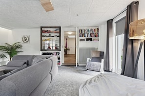 A modern living room with a grey sofa, a bookshelf, a radiator, and a window with curtains. - Cosy and modern house in peaceful setting (Otterup)