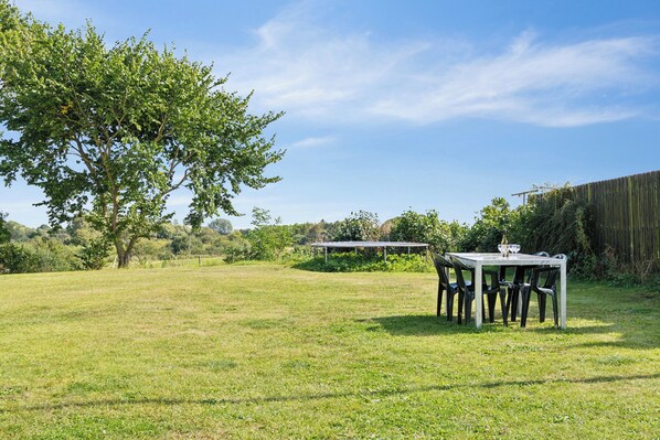 An outdoor dining area with a table and chairs, surrounded by a grassy field and trees.