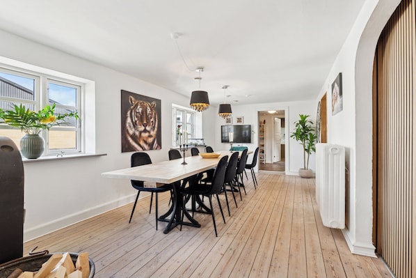 A modern kitchen with a wooden floor, a dining table with chairs, a large window, and a potted plant.