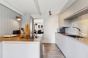 A modern kitchen with a central island, white cabinetry, and a view into the dining area. - Cosy and modern house in peaceful setting (Otterup)