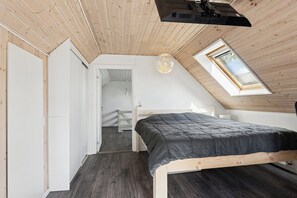 A room with a sloped ceiling, a bed with a dark mattress, a white wardrobe, and a skylight. - Cosy and modern house in peaceful setting (Otterup)