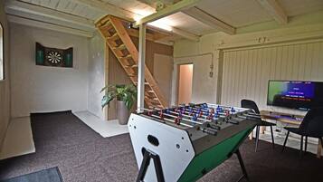A room with a foosball table, a dartboard, and a television.