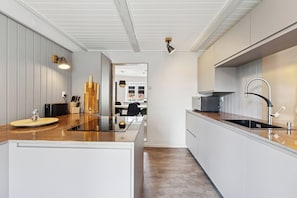 A modern kitchen with a central island, white cabinetry, and a view into the dining area. - Cosy and modern house in peaceful setting (Otterup)