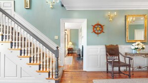 A staircase with white balusters and wooden steps, a wooden chair, a mirror with a gold frame, and a wall-mounted ship's wheel. - The Hill (Providence)