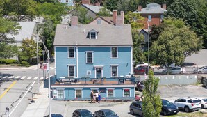 A two-story building with a blue exterior, a front porch with seating, and a visible street view. - The Hill (Providence)