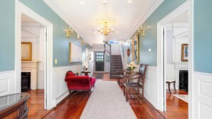 A hallway with a red velvet sofa, a wooden bench, and a white rug leading to a staircase. - The Hill (Providence)