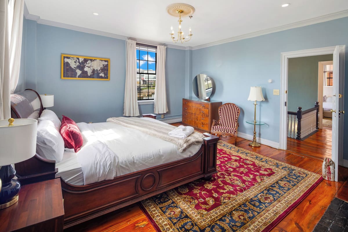 A bedroom with a large bed, a dresser, a chair, a lamp, and a rug.