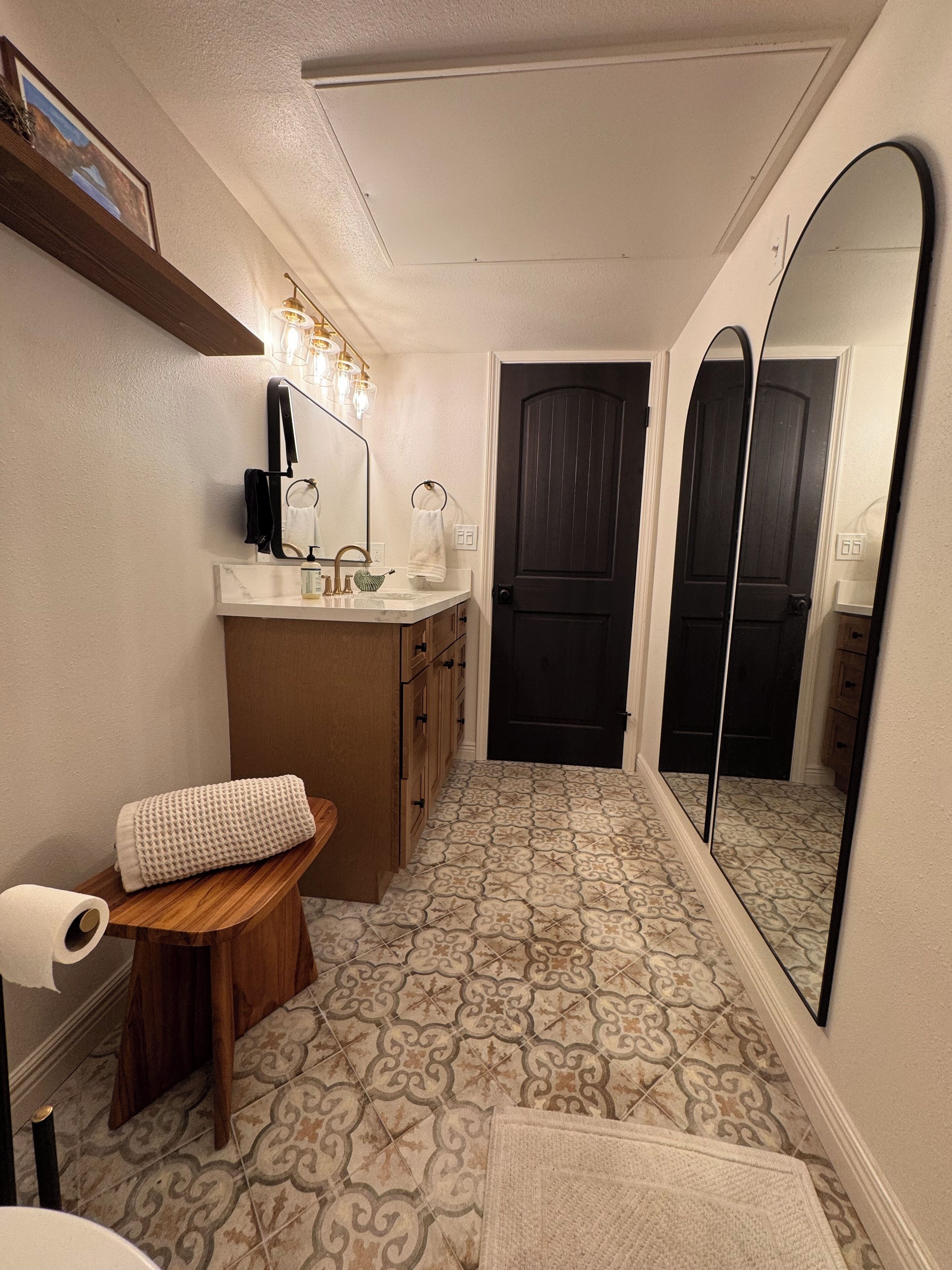 Une salle de bain avec un meuble-lavabo, un grand miroir, des carreaux de sol à motifs et un banc en bois.