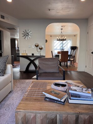 A modern living room with a sofa, a coffee table with books, a dining area with a chandelier, and a kitchen in the background. - Amazing Condo In Downtown Alhambra, 20 minutes to DTLA, 10 minutes to Pasadena (Alhambra)