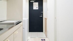 A narrow hallway with a black door, a white wall, and a small counter with a sink. - Daffitto Mitaka (Mitaka)