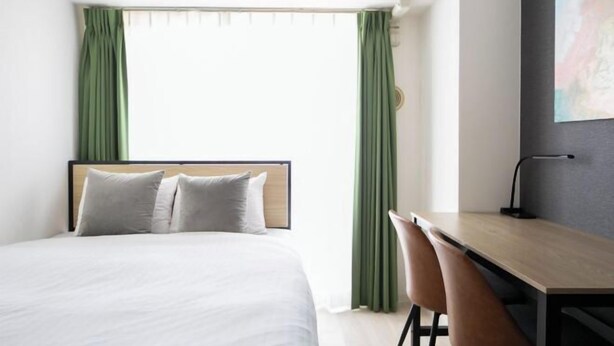 A hotel room with a bed, a desk, two chairs, and a window with curtains. - Daffitto Mitaka (Mitaka)