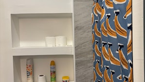A bathroom with a toilet, a shelf with toilet paper, a can of air freshener, and a shower curtain with a banana pattern. - 1 bedroom apartment across from Temple Hospital (Philadelphia)